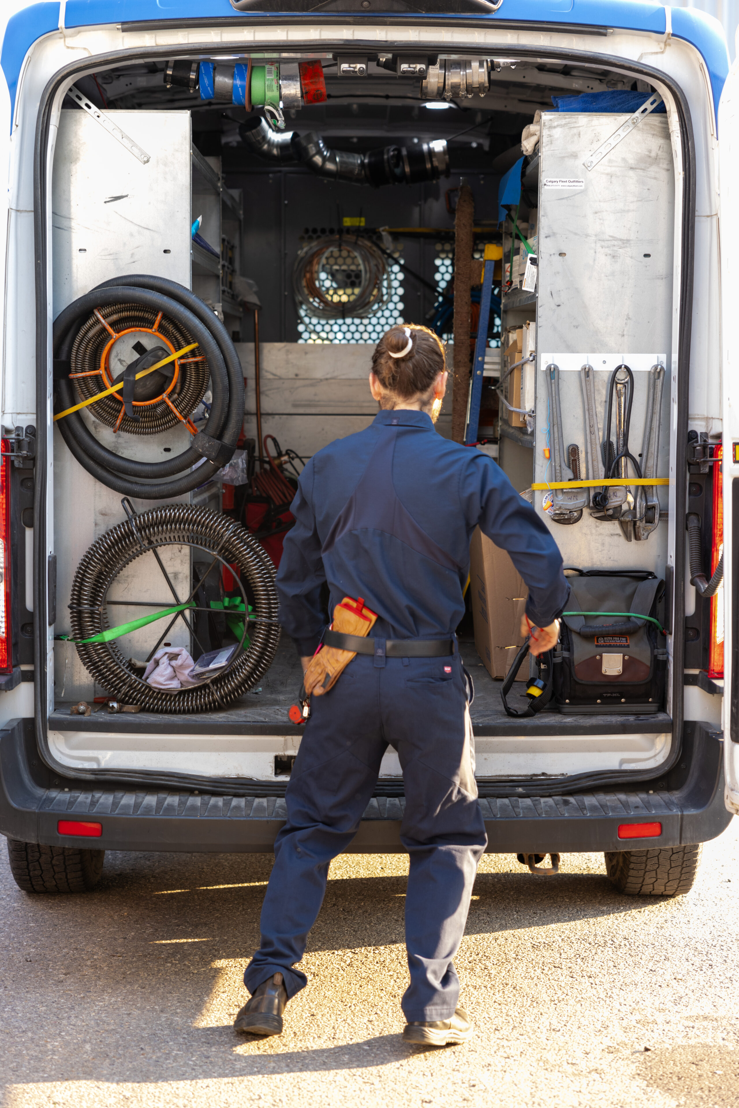 A worker standing at the back of a utility van that is well-organized and equipped for a HVAC Services